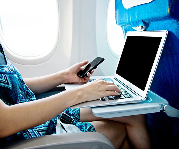 Image of an airline passenger working with a mobile device and a laptop.